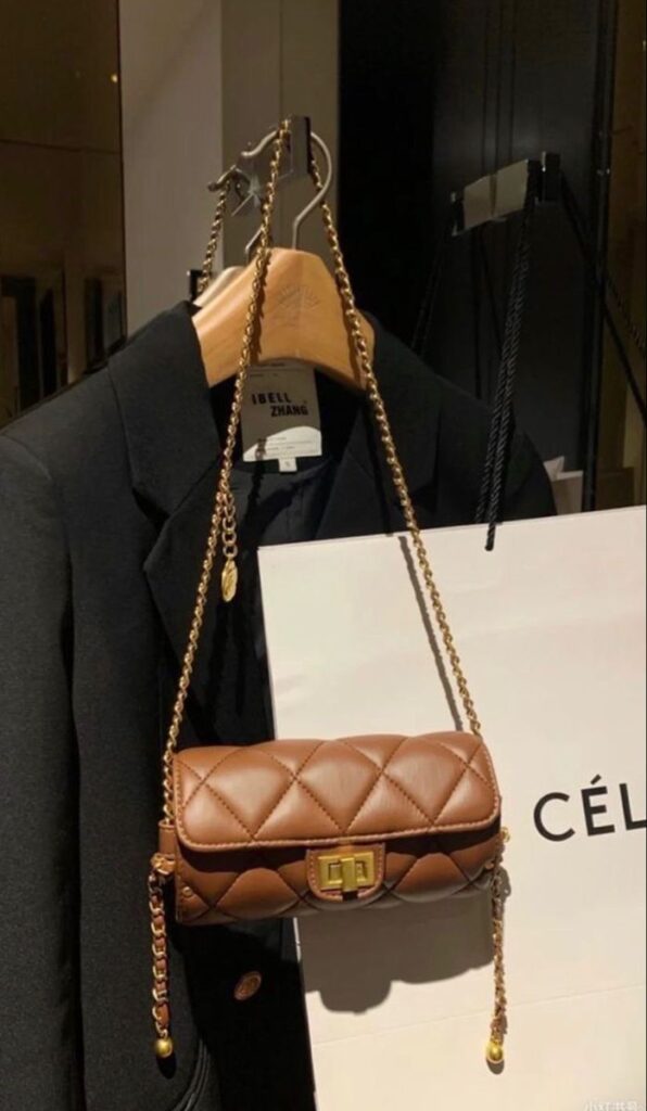 _ 78 Luxurious brown quilted handbag with gold chain strap hanging on a black coat in a chic showroom. | Sky Rye Design Luxurious brown quilted handbag with gold chain strap hanging on a black coat in a chic showroom.