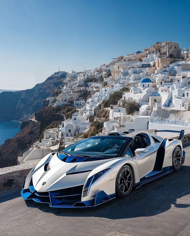 788f6ec0-53f3-4bdf-95b7-3452d1713c51 Luxury sports car parked with stunning Santorini backdrop, featuring white buildings and blue domes under a clear sky. | Sky Rye Design Luxury sports car parked with stunning Santorini backdrop, featuring white buildings and blue domes under a clear sky.