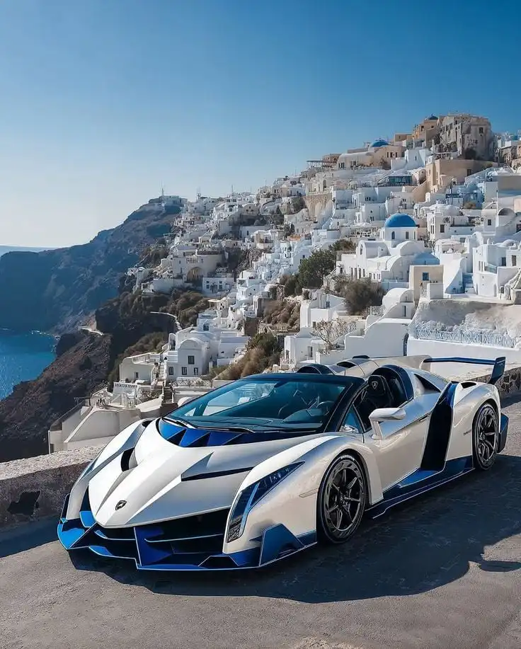 Luxury sports car parked with stunning Santorini backdrop, featuring white buildings and blue domes under a clear sky.