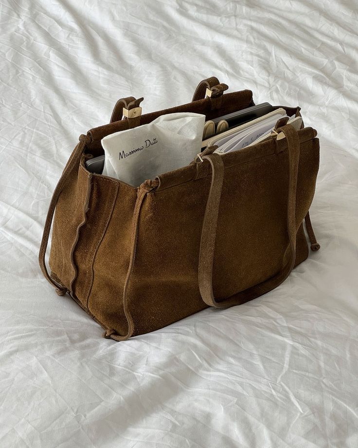 _ 79 Brown suede bag on white bedding, filled with books and a Massimo Dutti item. | Sky Rye Design Brown suede bag on white bedding, filled with books and a Massimo Dutti item.