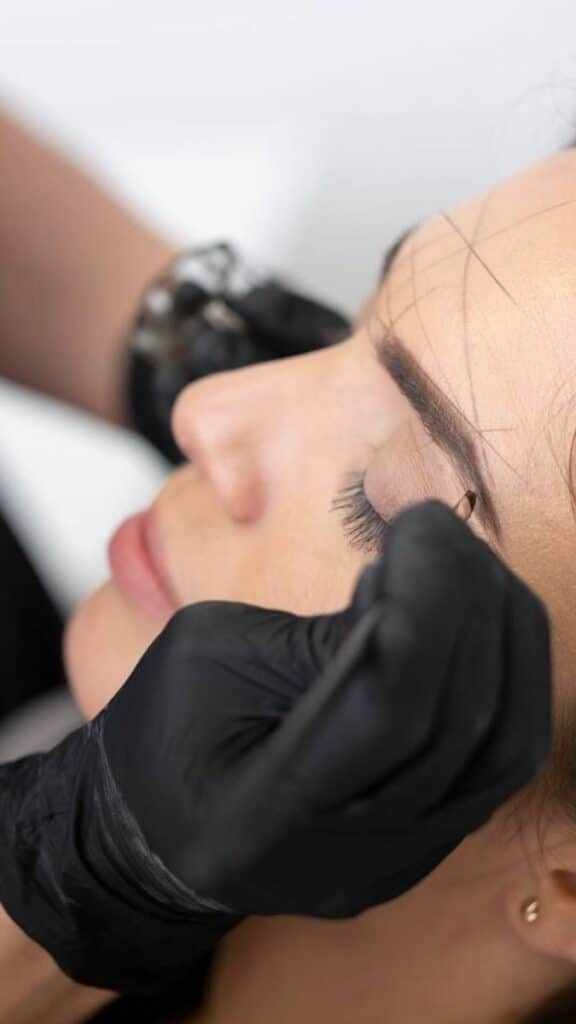 _ 8 Beautician applying eyebrow treatment with black gloves in a cosmetic procedure, close-up on closed eyes and precise work. | Sky Rye Design Beautician applying eyebrow treatment with black gloves in a cosmetic procedure, close-up on closed eyes and precise work.