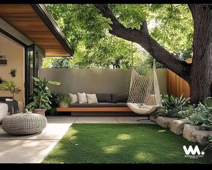 Cozy outdoor patio with hammock, sofa, and lush plants under a large tree, perfect for relaxing and enjoying nature.