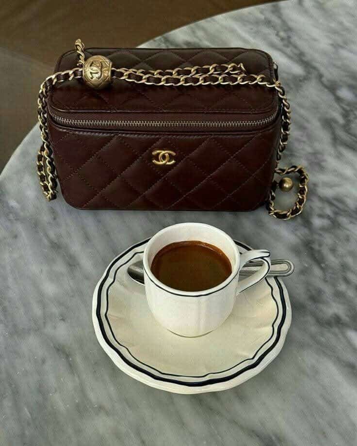 _ 80 Elegant brown quilted handbag with gold chain beside a cup of coffee on a marble table. Cozy luxury fashion and lifestyle. | Sky Rye Design Elegant brown quilted handbag with gold chain beside a cup of coffee on a marble table. Cozy luxury fashion and lifestyle.