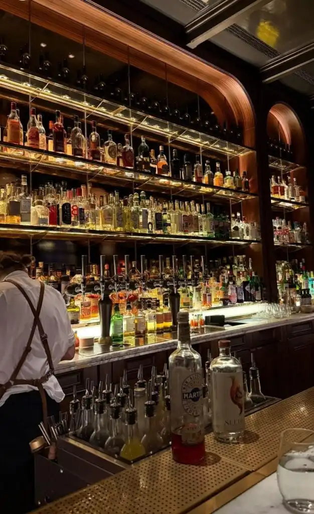 Elegant bar interior showcasing a wide variety of liquor bottles neatly arranged on shelves, with a bartender preparing drinks.