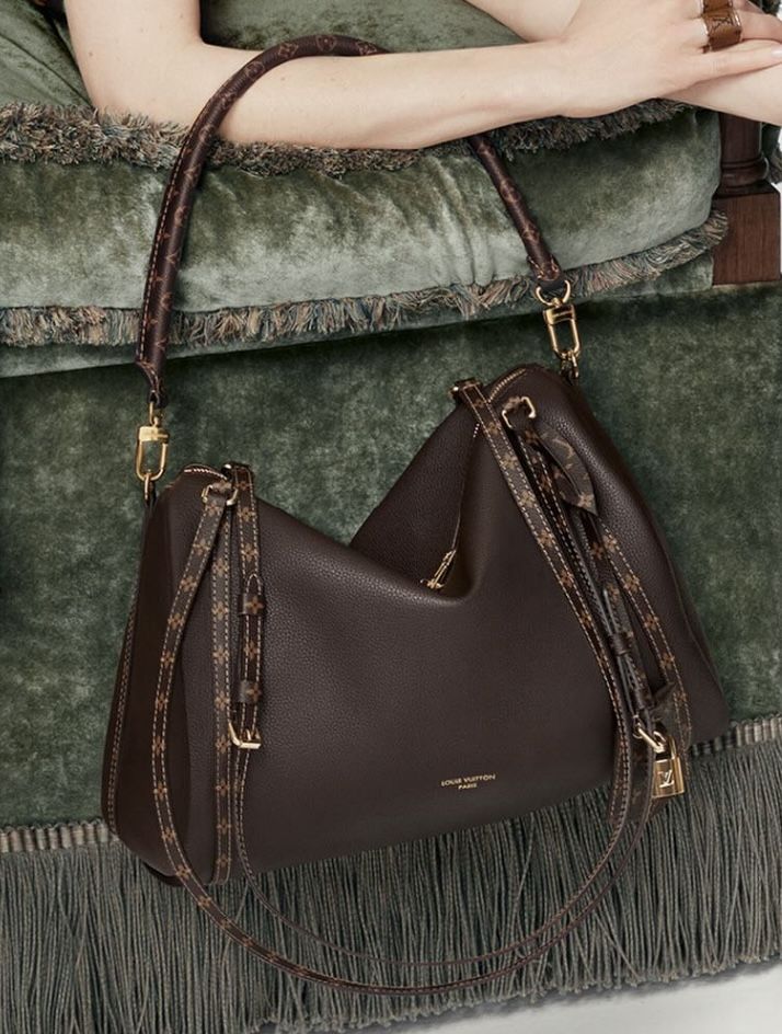 Screenshot Luxurious brown leather handbag with gold accents on a green velvet couch, featuring a stylish design and adjustable straps. | Sky Rye Design Luxurious brown leather handbag with gold accents on a green velvet couch, featuring a stylish design and adjustable straps.