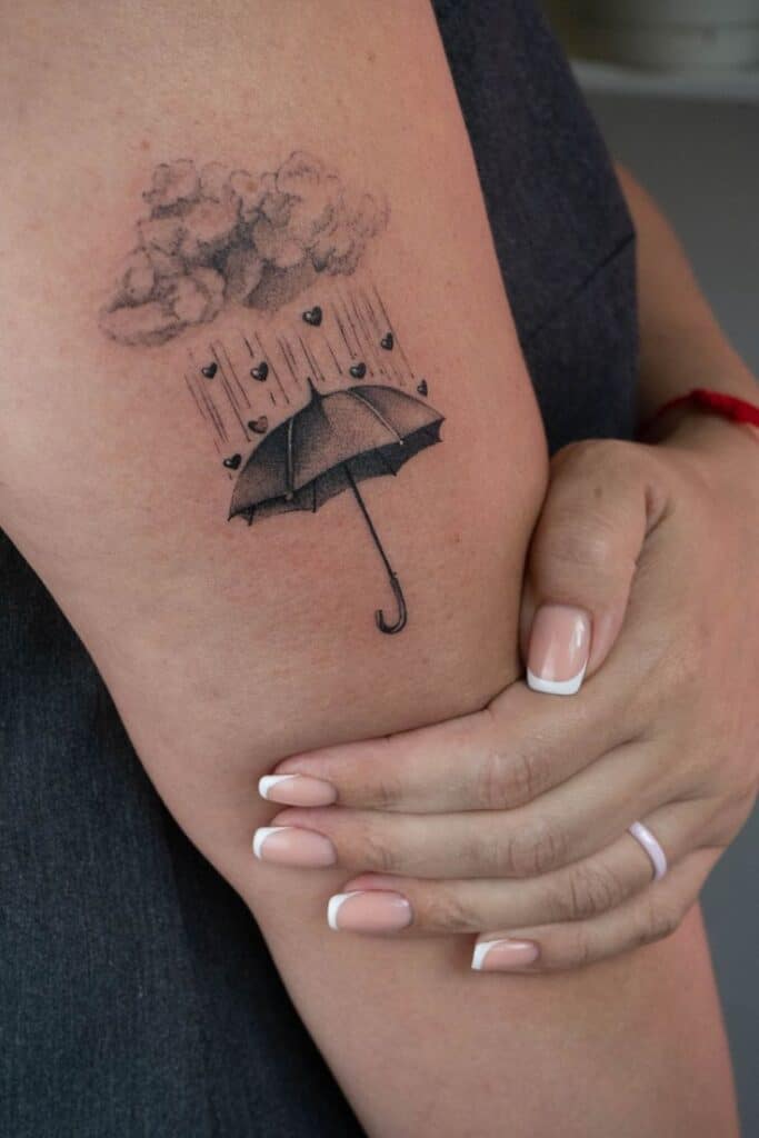 83ca466d-1f5c-43d6-97b8-04ce5af83193 Tattoo of umbrella under heart raindrops from a cloud on an upper arm, showcasing creative body art design and intricate details. | Sky Rye Design Tattoo of umbrella under heart raindrops from a cloud on an upper arm, showcasing creative body art design and intricate details.