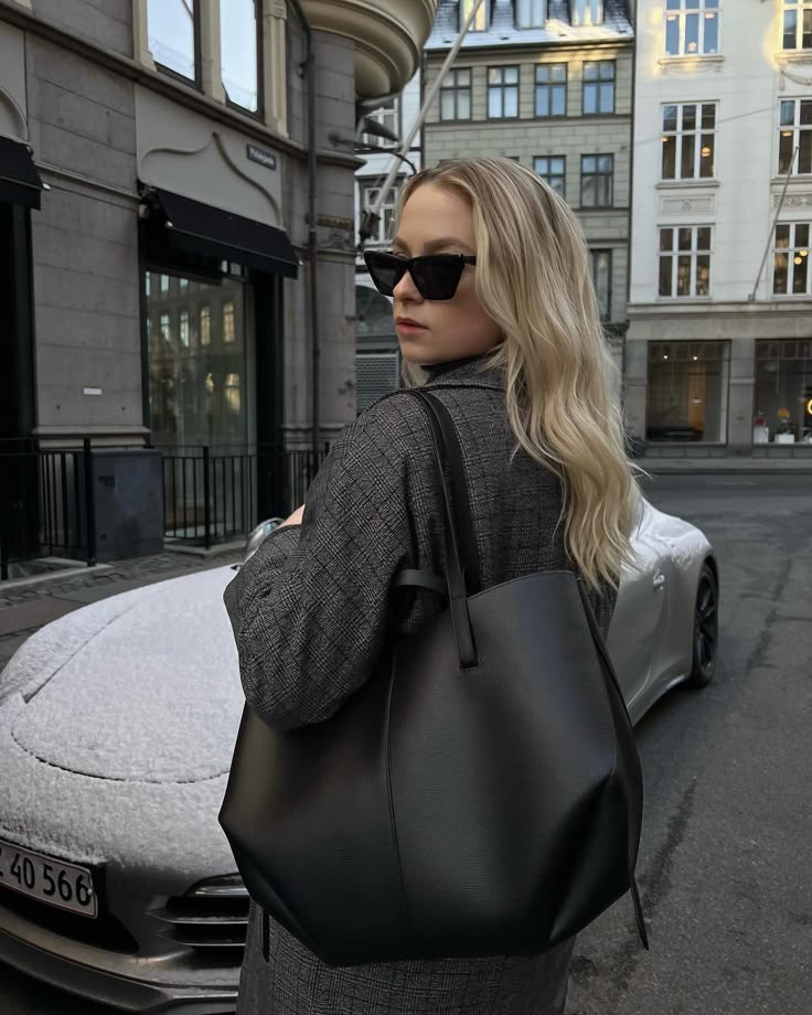 _ 84 Blonde woman in sunglasses with a black bag, standing in a city street beside a parked car on a snowy day. | Sky Rye Design Blonde woman in sunglasses with a black bag, standing in a city street beside a parked car on a snowy day.