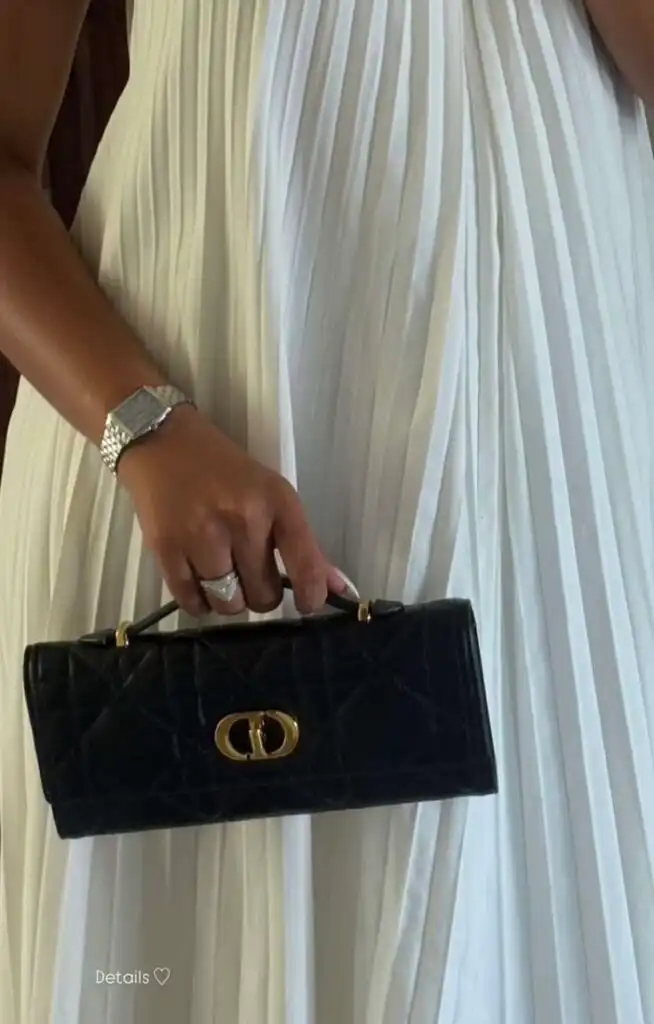 Woman in white dress holding a black designer clutch and wearing a silver watch and ring, showcasing elegant style and fashion details.