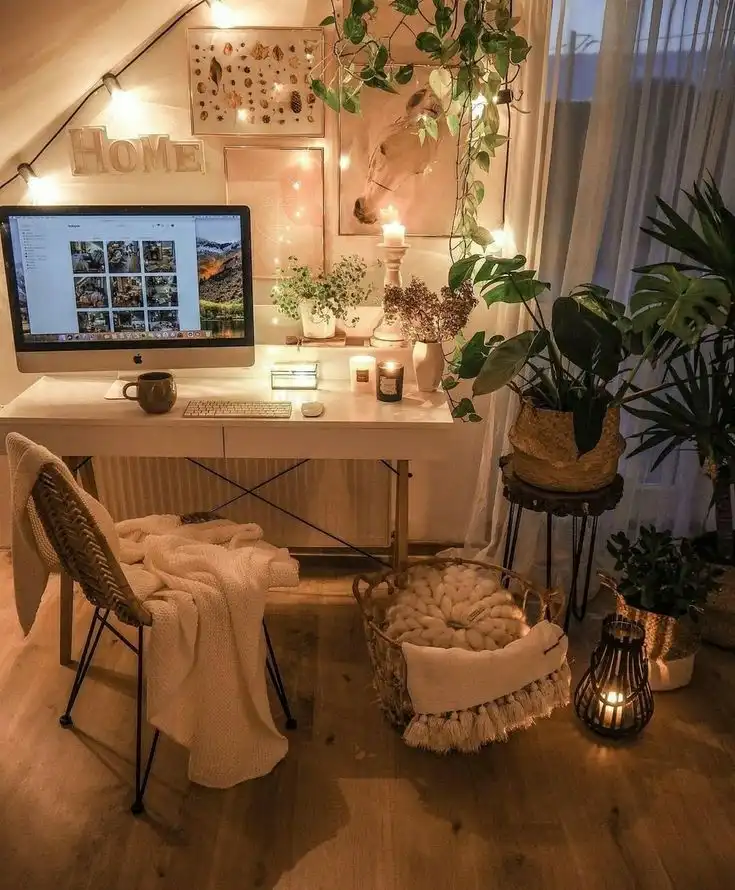 Cozy home office with computer, plants, candles, and warm lighting, creating a relaxing and inviting workspace atmosphere.
