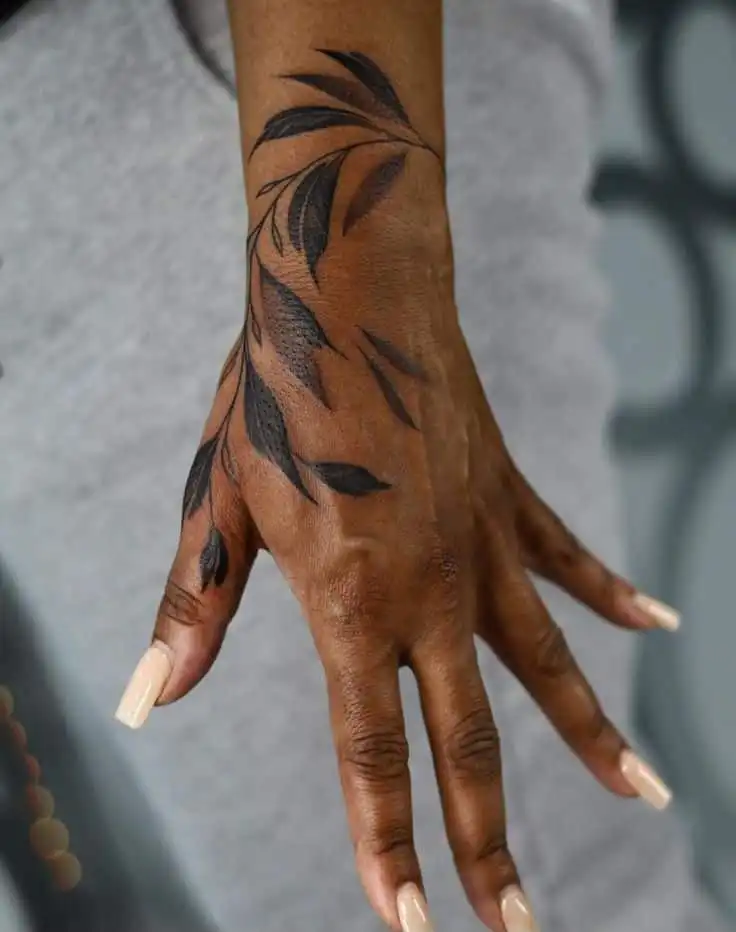 Intricate black leaf tattoo on hand with neutral nails, showcasing artistic detail and modern tattoo design for personal expression.