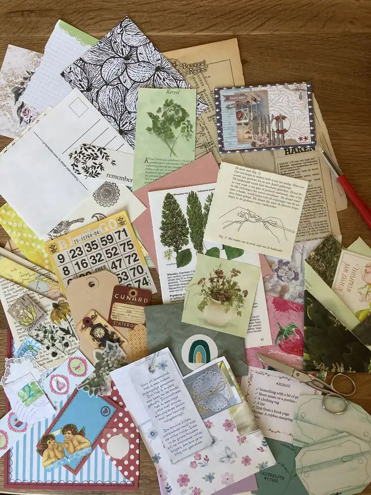 Flat lay of a collection of vintage paper ephemera, including postcards, floral illustrations, and decorative tags on a wooden surface.