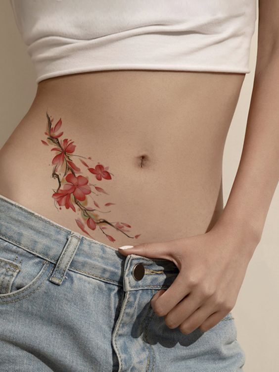 _ 98 Floral tattoo on woman's hip and waist, wearing jeans and a white crop top. Elegant red flowers design for body art inspiration. | Sky Rye Design Floral tattoo on woman's hip and waist, wearing jeans and a white crop top. Elegant red flowers design for body art inspiration.