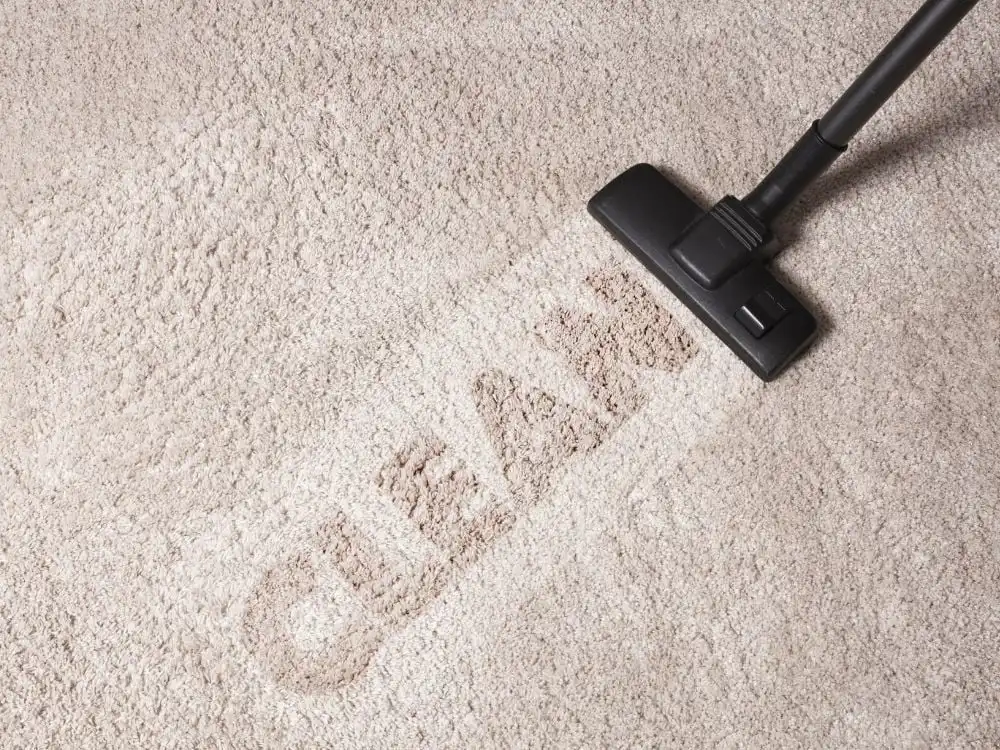 Vacuum cleaner removing dirt from a beige carpet, revealing the word CLEAN in contrasting texture. Ideal for cleaning