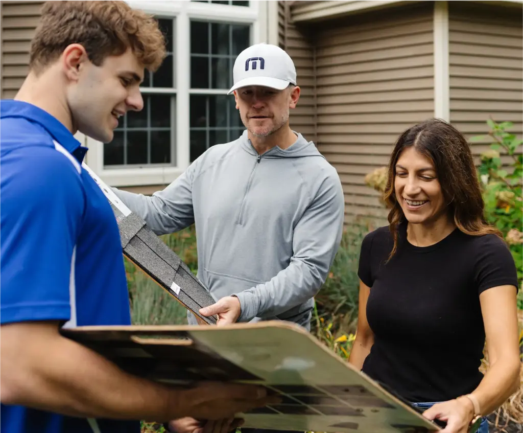 A-friendly-roofing-contractor-talking-with-two-homeowners-in-the-font-lawn-of-a-nice-home-that-needs-a-new-roof Three people discuss roofing materials outside a house, showcasing teamwork in home renovation projects. | Sky Rye Design Three people discuss roofing materials outside a house, showcasing teamwork in home renovation projects.