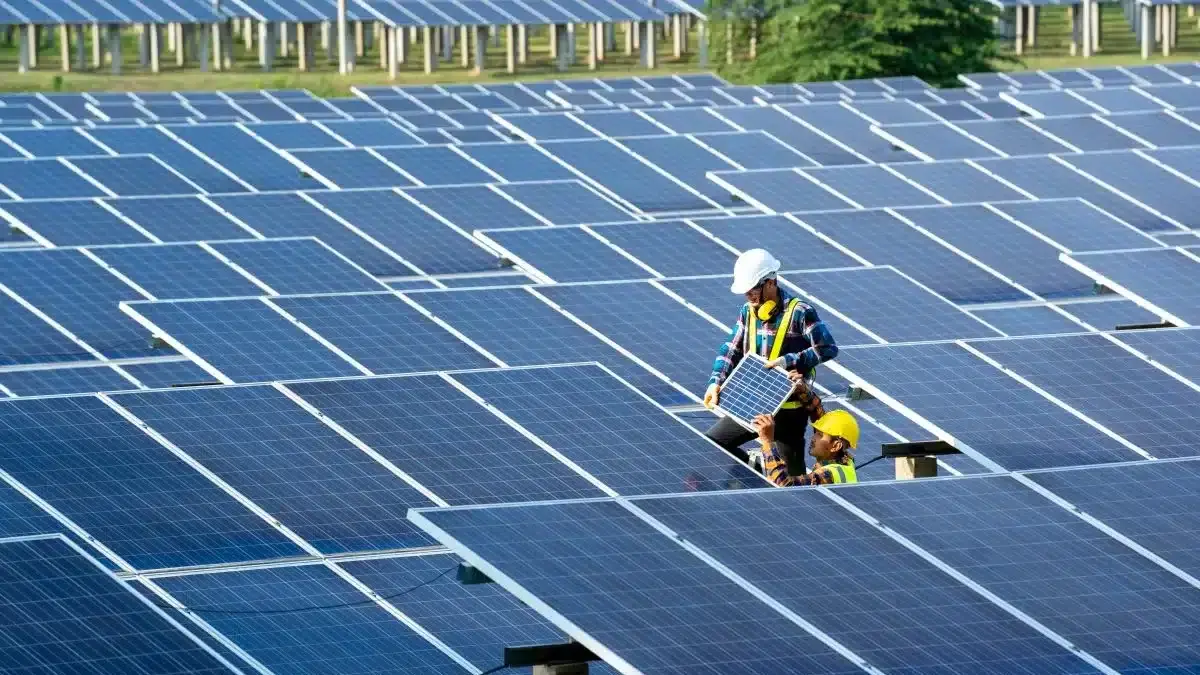 Technicians installing solar panels in a large photovoltaic farm, harnessing renewable energy under bright sunlight.