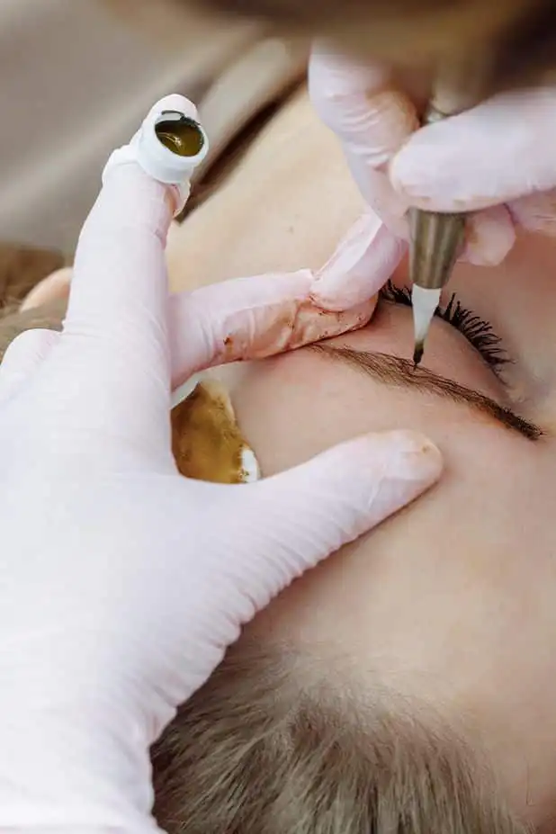 Are People Still Getting Their Eyebrows Microbladed_ Professional microblading procedure on eyebrows, close-up view with precision tools, enhancing natural brow appearance for beauty treatment. | Sky Rye Design Professional microblading procedure on eyebrows, close-up view with precision tools, enhancing natural brow appearance for beauty treatment.