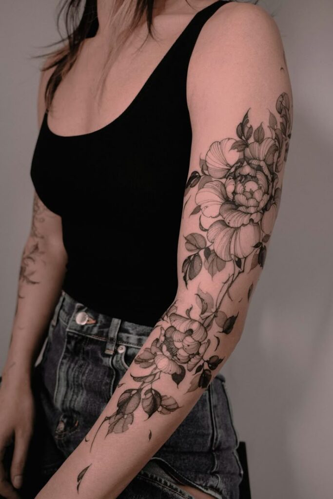 Artys Floral Fantasies_ How This Berlin-Based Artist Redefined Botanical Tattoos _ iNKPPL Ornate floral tattoo design on woman's arm in black ink, wearing black tank top and denim shorts. Tattoos, body art, floral design. | Sky Rye Design Ornate floral tattoo design on woman's arm in black ink, wearing black tank top and denim shorts. Tattoos, body art, floral design.
