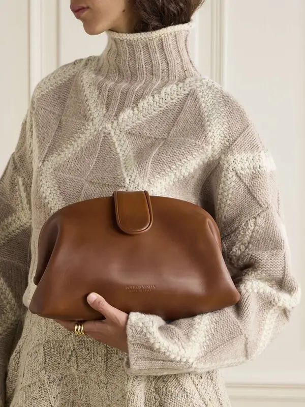 BOTTEGA VENETA _ Woman in cozy knit sweater holds a stylish brown leather clutch, showcasing chic autumn fashion. | Sky Rye Design Woman in cozy knit sweater holds a stylish brown leather clutch, showcasing chic autumn fashion.