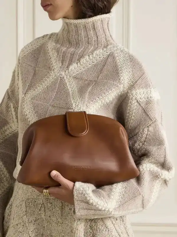 Woman in cozy knit sweater holds a stylish brown leather clutch, showcasing chic autumn fashion.