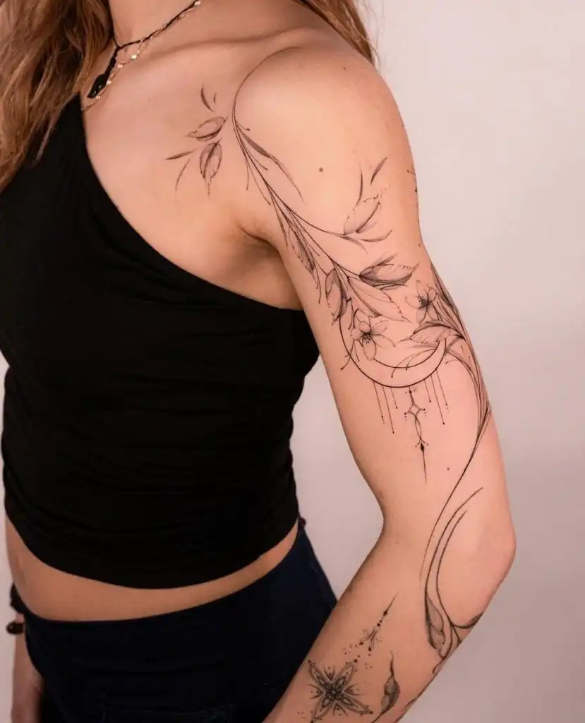 Intricate floral and star tattoos on woman's arm, wearing a black top and necklace, showcasing detailed art on skin.