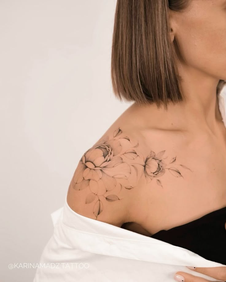 Floral shoulder tattoo on woman with short brown hair, showcasing delicate peonies and leaves, against a neutral background.