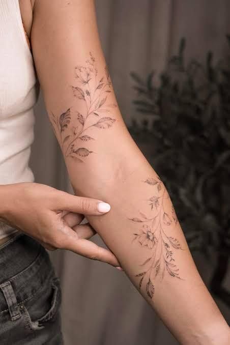 Delicate floral tattoos on a person's arm, showcasing intricate leaf and flower designs, emphasizing elegance and personal style.