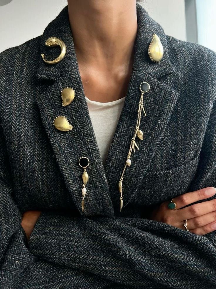 Close-up of a black herringbone blazer adorned with unique gold brooches, featuring moon and teardrop shapes, adding elegance and style.
