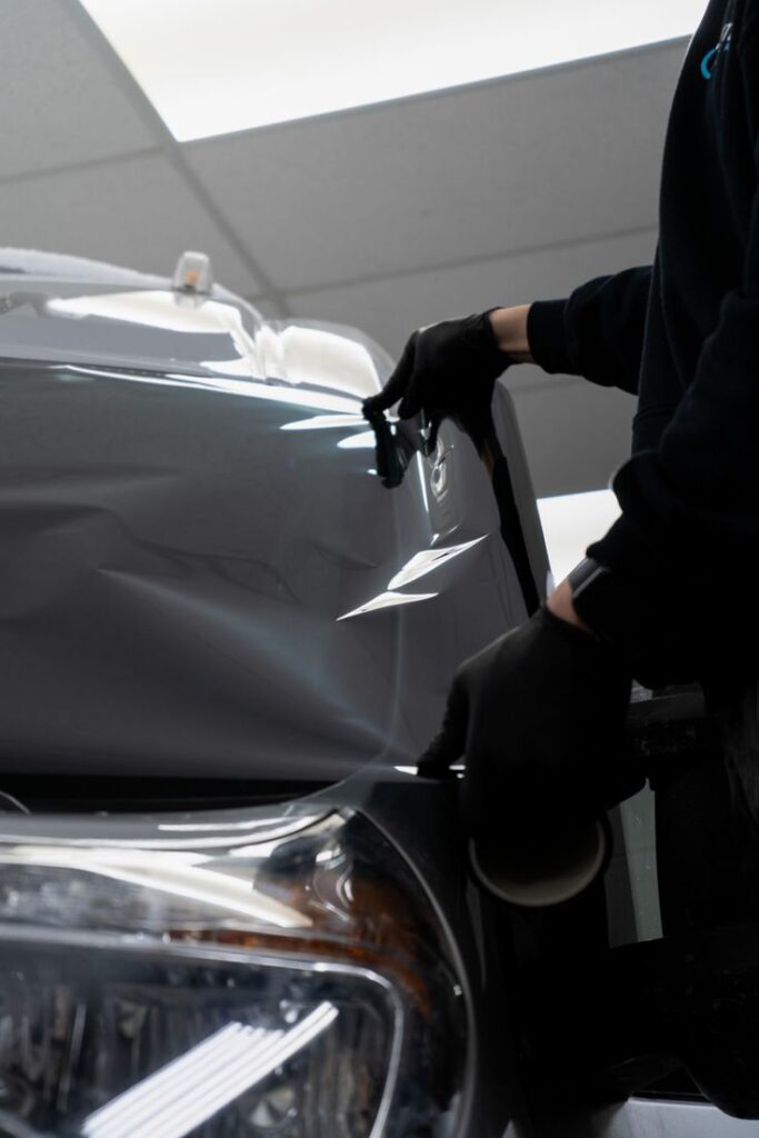 CAR WRAP is a FANTASTIC TOOL Person applying protective film to car headlight in workshop, enhancing vehicle safety and appearance. | Sky Rye Design Person applying protective film to car headlight in workshop, enhancing vehicle safety and appearance.