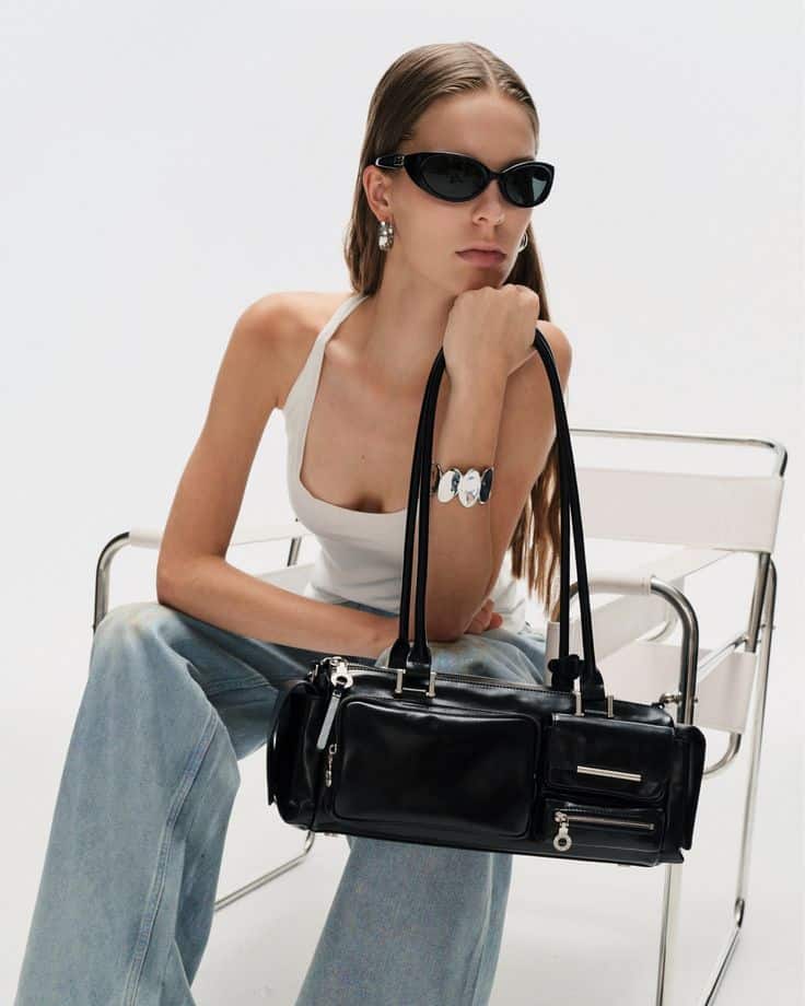 Capture Multipocket Bag Refined yet functional Fashionable woman in sunglasses with a sleek black handbag, wearing a white tank top and jeans, sitting stylishly on a modern chair. | Sky Rye Design Fashionable woman in sunglasses with a sleek black handbag, wearing a white tank top and jeans, sitting stylishly on a modern chair.