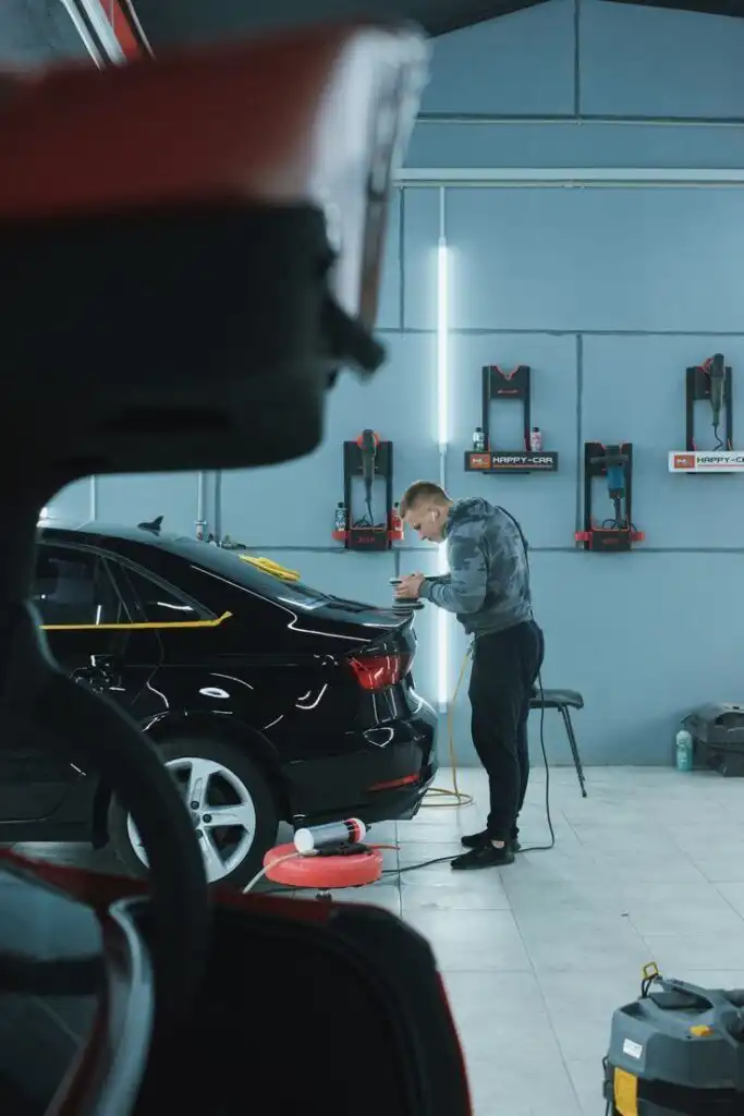 Man detailing a black car in an auto workshop, using tools for precision car care.