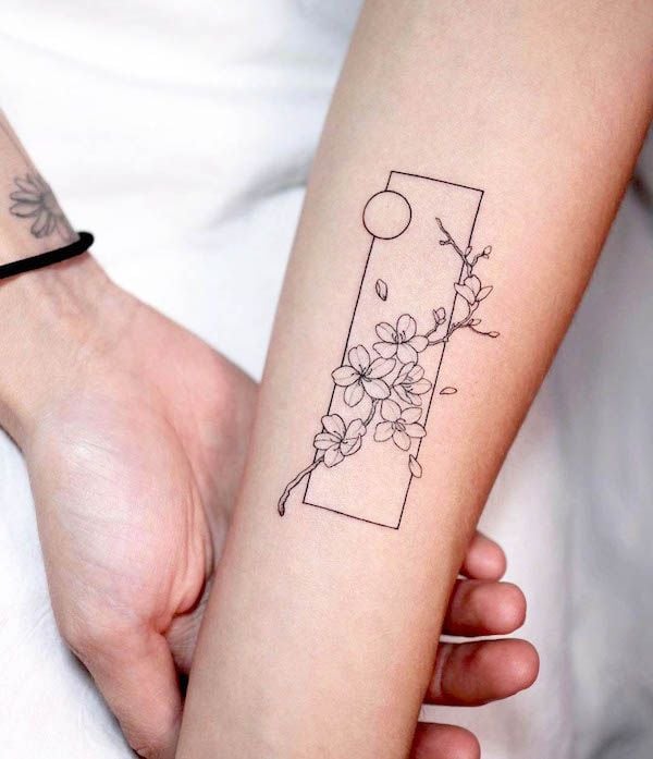Minimalist cherry blossom tattoo with geometric design on a forearm, featuring delicate branches and flowers.
