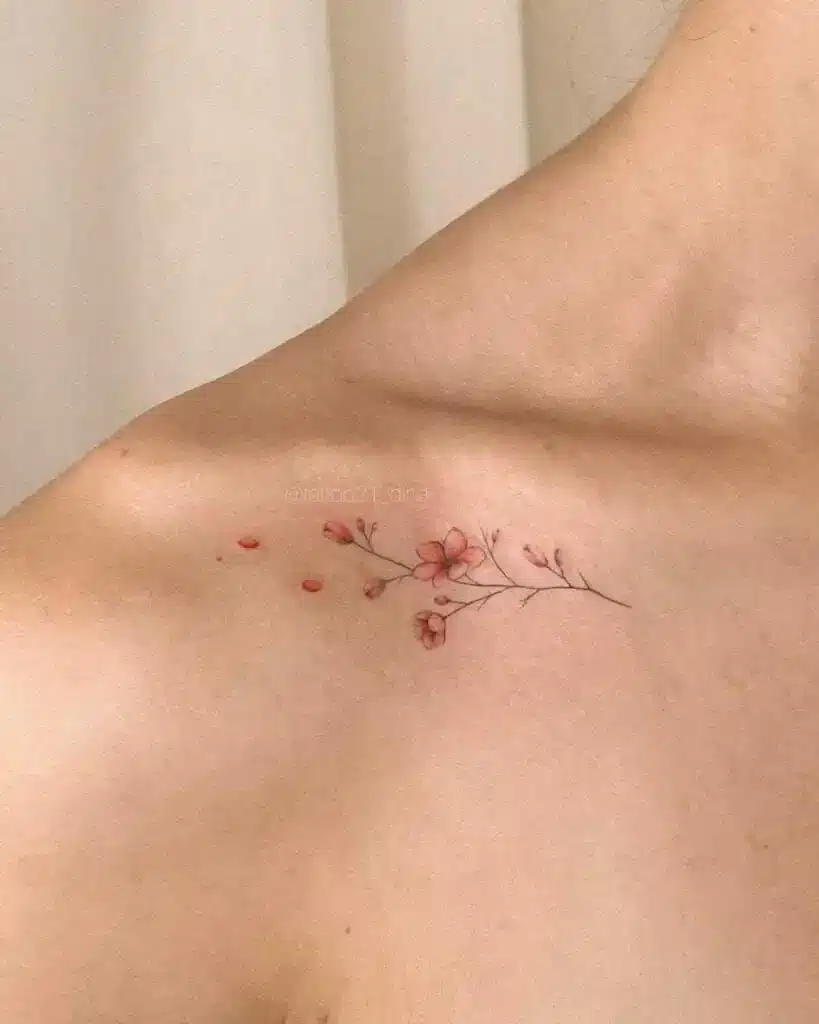 Delicate floral tattoo on shoulder featuring pink blossoms and subtle branches, elegantly designed for minimalist style lovers.