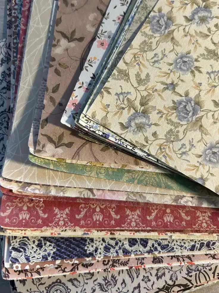 A stack of decorative scrapbook paper with floral and patterned designs in various colors, perfect for crafting and DIY projects.