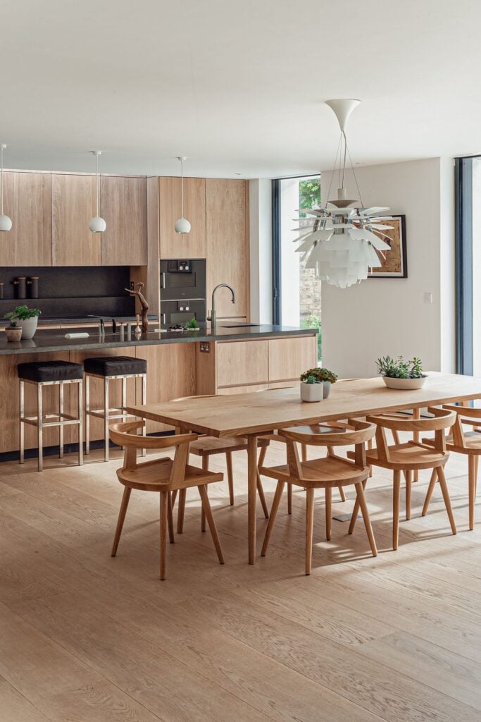 Modern kitchen with wooden cabinets, central island, sleek dining table, and unique pendant lighting for a cozy, stylish space.