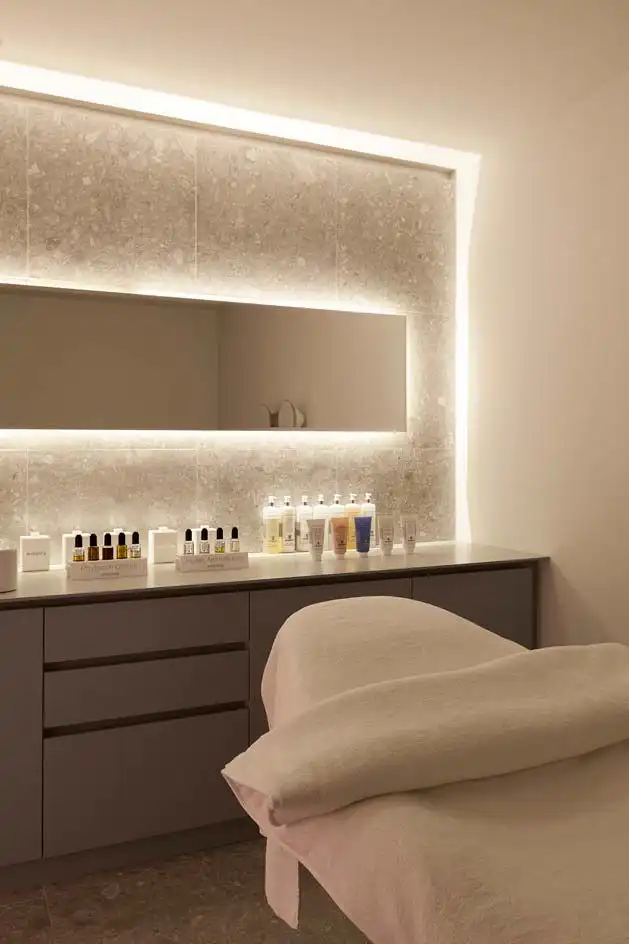Spa treatment room with a modern aesthetic, featuring a massage table, sleek gray cabinets, and a variety of skincare products on display.