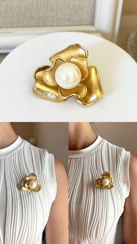 Elegant gold flower brooch with pearl center on white pleated dress, showcasing timeless fashion accessories and sophisticated style.