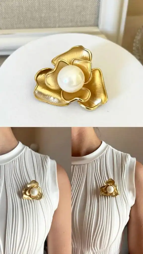 Elegant gold flower brooch with pearl center on white pleated dress, showcasing timeless fashion accessories and sophisticated style.
