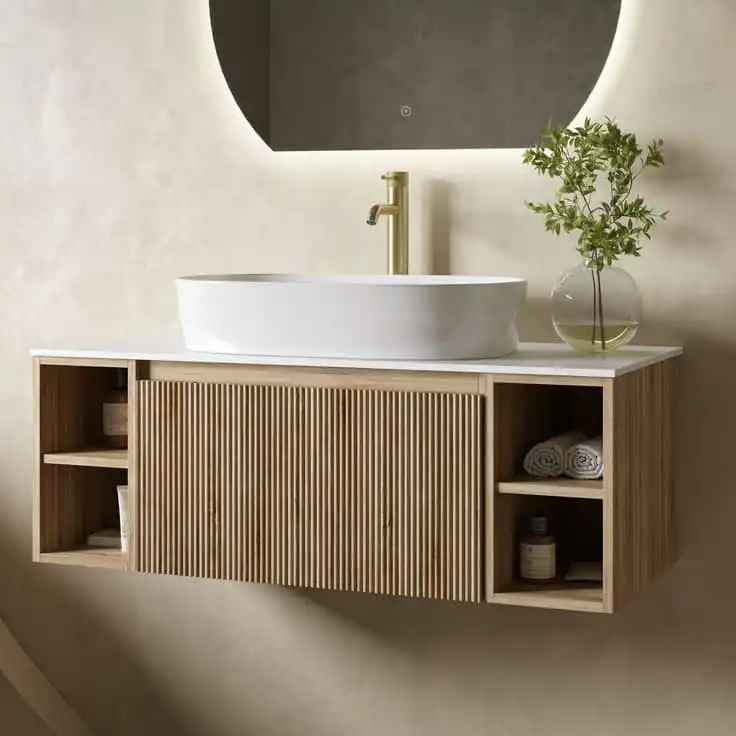 Modern bathroom with a wooden floating vanity, vessel sink, and green plant in a glass vase, under a glowing round mirror.