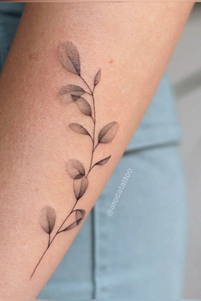 Minimalist branch tattoo with delicate leaves on a forearm, showcasing elegant line art and shading for a subtle, nature-inspired design.