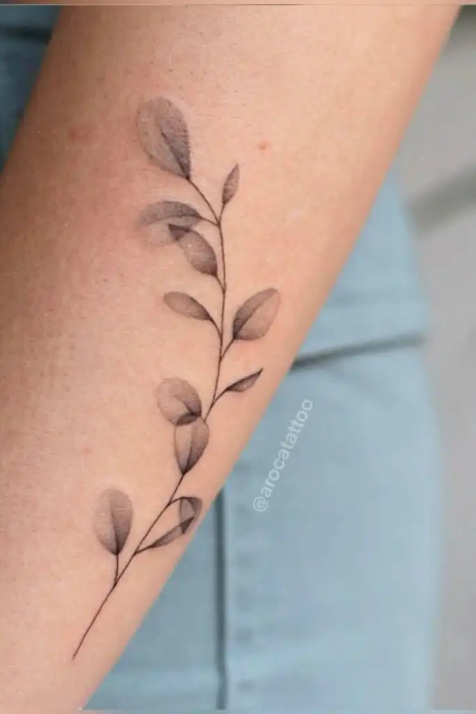 Minimalist branch tattoo with delicate leaves on a forearm, showcasing elegant line art and shading for a subtle, nature-inspired design.