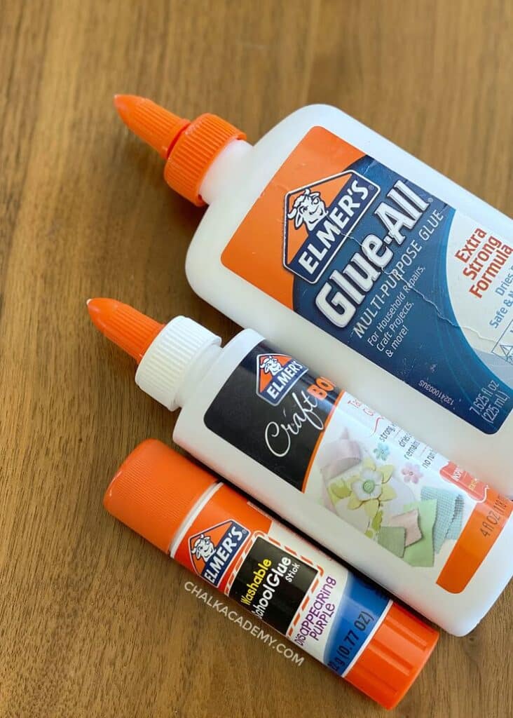 Favorite School and Art Supplies for Bilingual Kids Three Elmer's glue types on a wooden surface: multi-purpose glue, craft glue, and washable school glue stick. | Sky Rye Design Three Elmer's glue types on a wooden surface: multi-purpose glue, craft glue, and washable school glue stick.