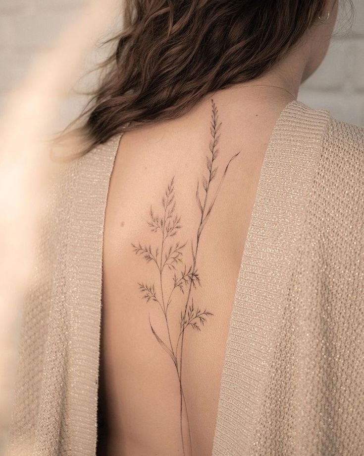 Delicate floral tattoo on woman's back, wearing knit sweater, highlighting minimalist botanical design.