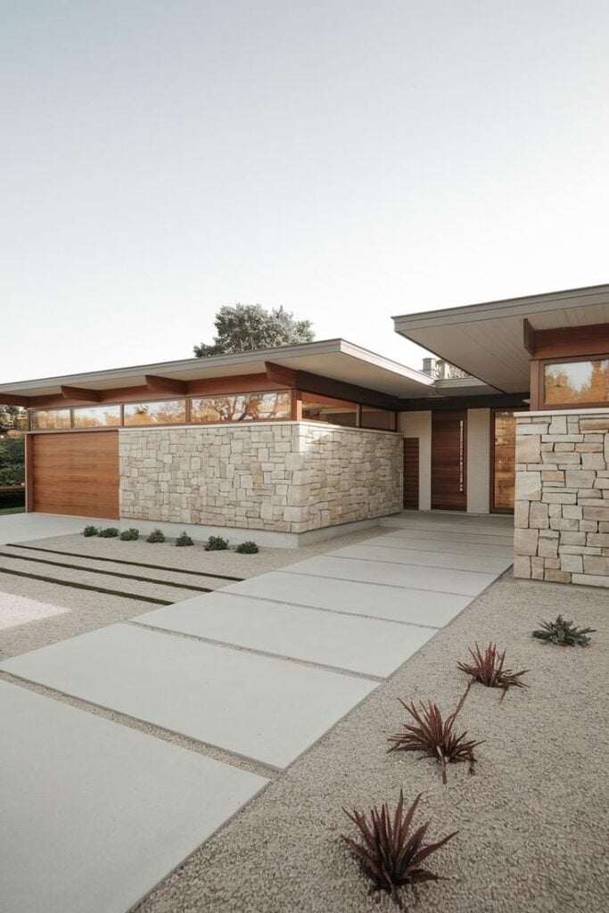 Modern mid-century home with sleek lines, stone facade, and minimalist landscaping under a clear sky. Ideal for architecture enthusiasts.