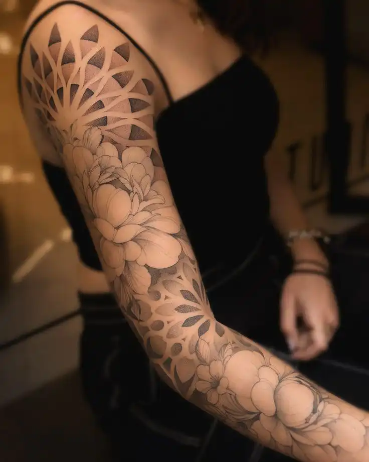 Intricate full sleeve tattoo featuring floral and geometric designs on a woman's arm, showcasing detailed black and gray artistry.