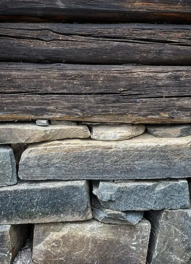 A close-up of rustic wooden logs stacked above a stone foundation, showcasing natural textures and construction materials.