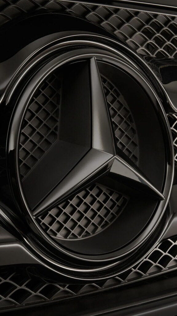 Close-up of a shiny black car grille with a prominent three-pointed star emblem, showcasing luxury and sleek automotive