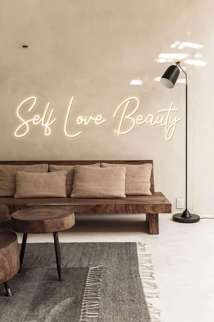 HDJSign - Self Love Beauty Home Decor Neon Sign - 26in _ Warm White Modern minimalist room with Self Love Beauty neon sign above a cozy wooden sofa, neutral cushions, round tables, and a floor lamp. | Sky Rye Design Modern minimalist room with Self Love Beauty neon sign above a cozy wooden sofa, neutral cushions, round tables, and a floor lamp.
