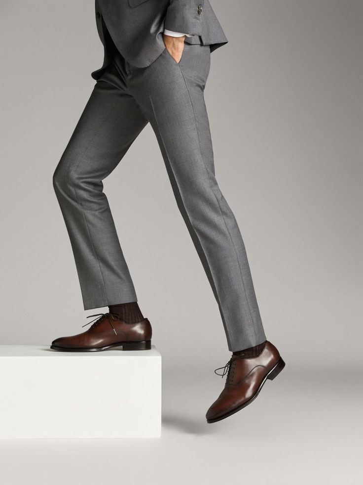 Person in gray suit wearing brown dress shoes, standing on a white platform, showcasing elegant footwear style with