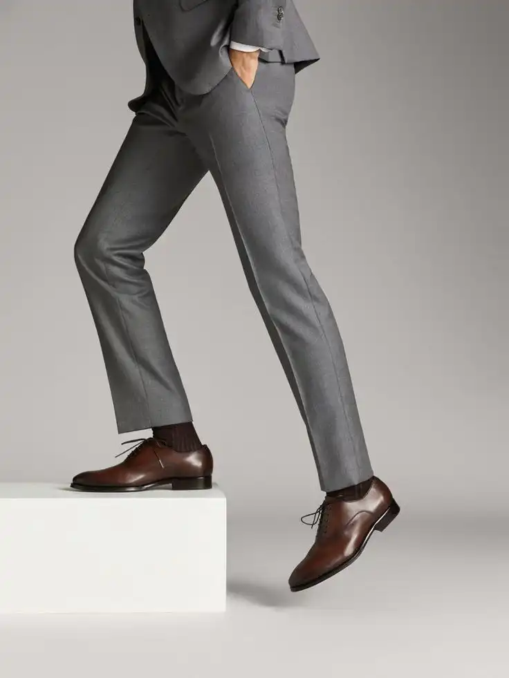 Person in gray suit wearing brown dress shoes, standing on a white platform, showcasing elegant footwear style with