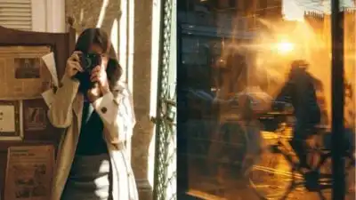 Woman in a trench coat takes a photo with a vintage camera. Golden sunset reflects on a window showing a cyclist in motion.